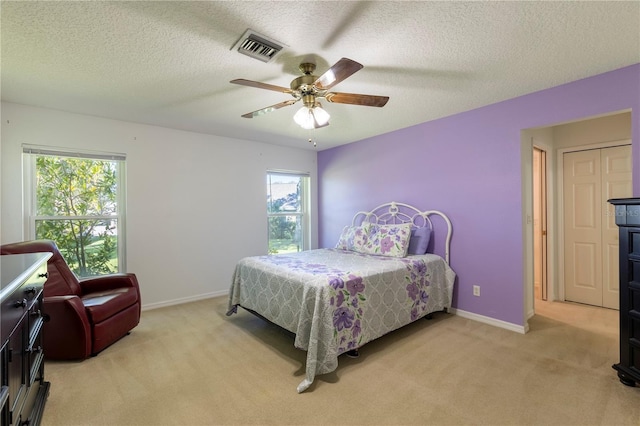 bedroom featuring ceiling fan, light colored carpet, a textured ceiling, and multiple windows