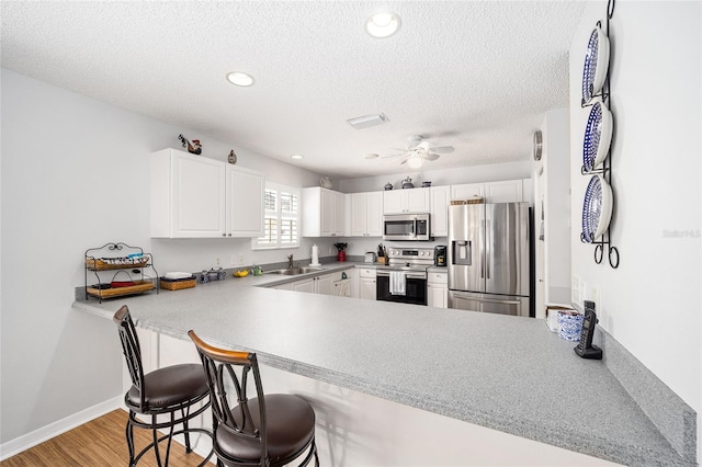 kitchen featuring light hardwood / wood-style flooring, ceiling fan, white cabinetry, kitchen peninsula, and stainless steel appliances