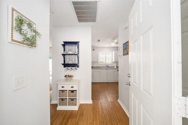 hallway with light hardwood / wood-style flooring, a textured ceiling, and sink