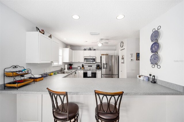 kitchen with kitchen peninsula, a kitchen breakfast bar, stainless steel appliances, ceiling fan, and white cabinetry