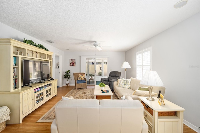 living room featuring ceiling fan, a textured ceiling, and light wood-type flooring