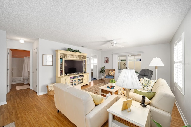 living room featuring ceiling fan, light wood-type flooring, and a textured ceiling