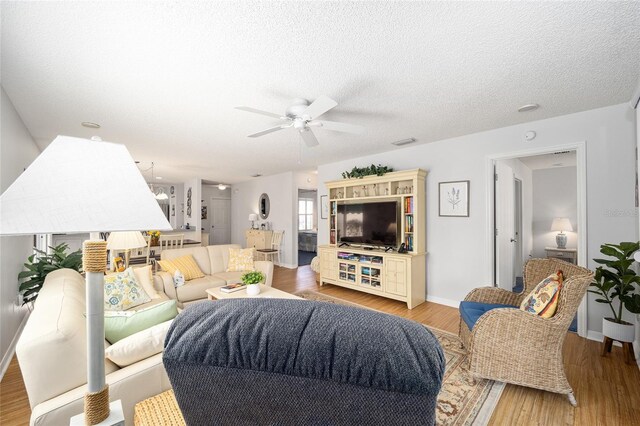 living room with a textured ceiling, light wood-type flooring, and ceiling fan