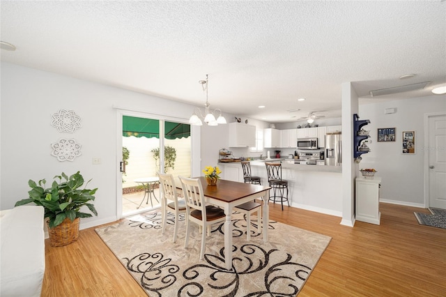 dining space featuring ceiling fan with notable chandelier, a textured ceiling, and light hardwood / wood-style flooring