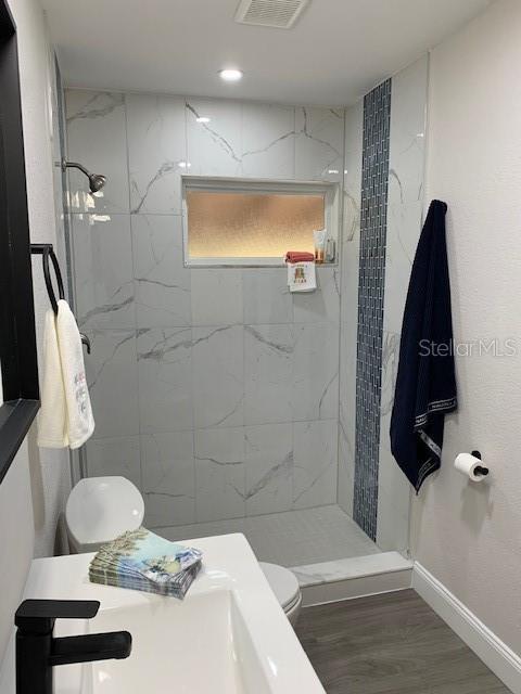 bathroom with a tile shower, hardwood / wood-style flooring, and toilet