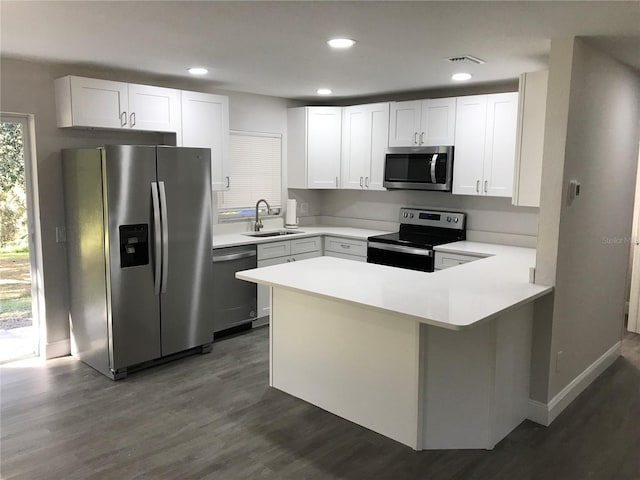 kitchen featuring visible vents, a peninsula, dark wood-style flooring, a sink, and stainless steel appliances