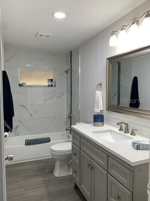 bathroom with visible vents, toilet, wood finished floors, vanity, and  shower combination