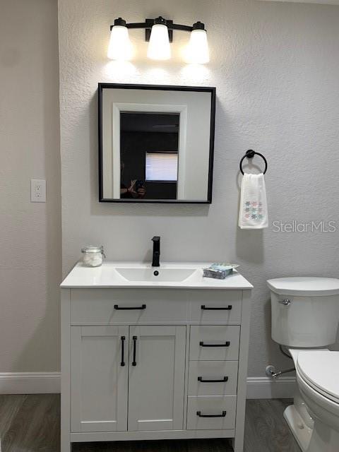 half bathroom featuring toilet, vanity, baseboards, and wood finished floors