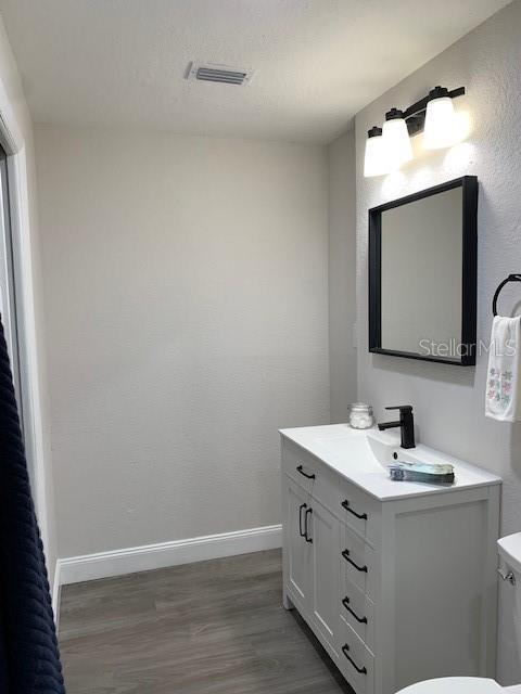 bathroom with visible vents, baseboards, toilet, wood finished floors, and vanity