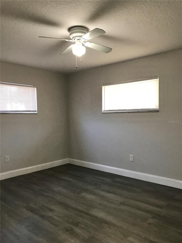 empty room featuring a ceiling fan, dark wood-style floors, baseboards, and a textured ceiling