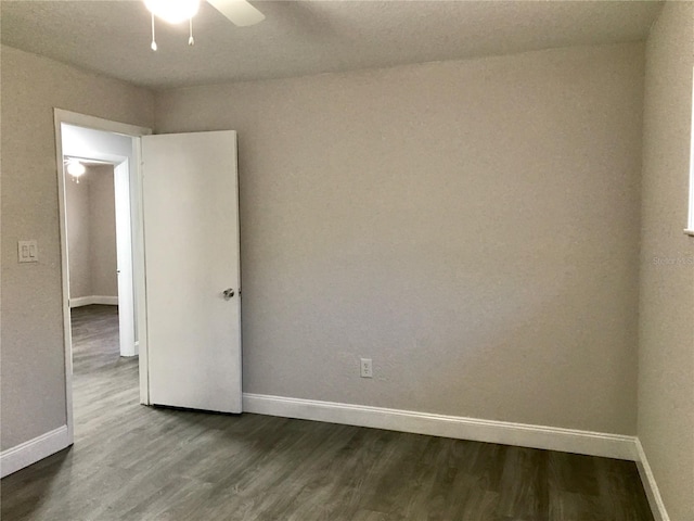 spare room featuring dark wood-type flooring, a ceiling fan, and baseboards