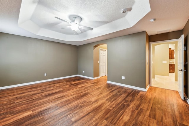 unfurnished room featuring a textured ceiling, ceiling fan, a tray ceiling, and dark hardwood / wood-style floors