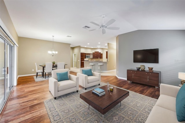 living room with ceiling fan with notable chandelier, wood-type flooring, and lofted ceiling