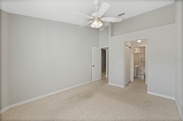 unfurnished bedroom featuring ceiling fan, light colored carpet, and ensuite bath