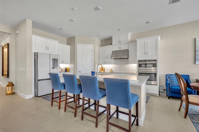 kitchen featuring a kitchen island with sink, white cabinetry, stainless steel double oven, and white refrigerator