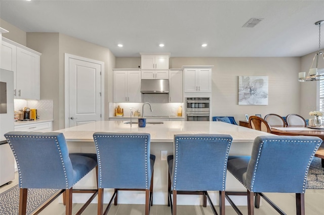 kitchen with white cabinets, decorative light fixtures, an island with sink, and a breakfast bar