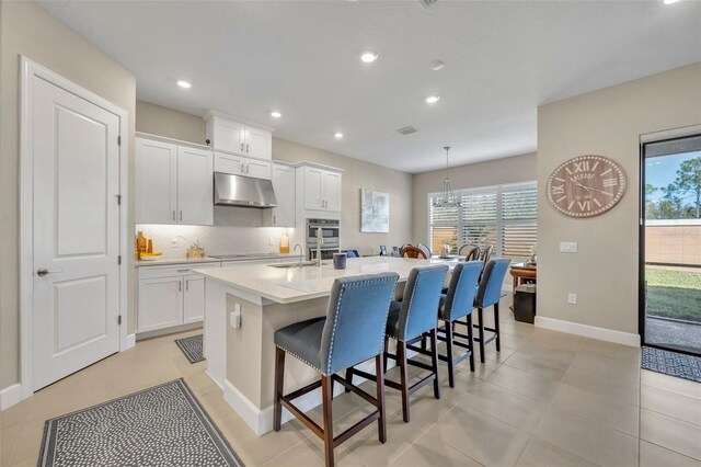 kitchen featuring white cabinetry, a kitchen island with sink, a breakfast bar, and hanging light fixtures