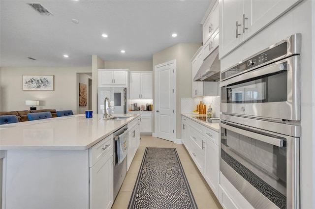 kitchen with white cabinets, sink, light tile patterned floors, an island with sink, and stainless steel appliances