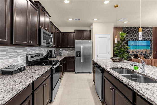 kitchen featuring appliances with stainless steel finishes, light stone counters, dark brown cabinetry, sink, and hanging light fixtures