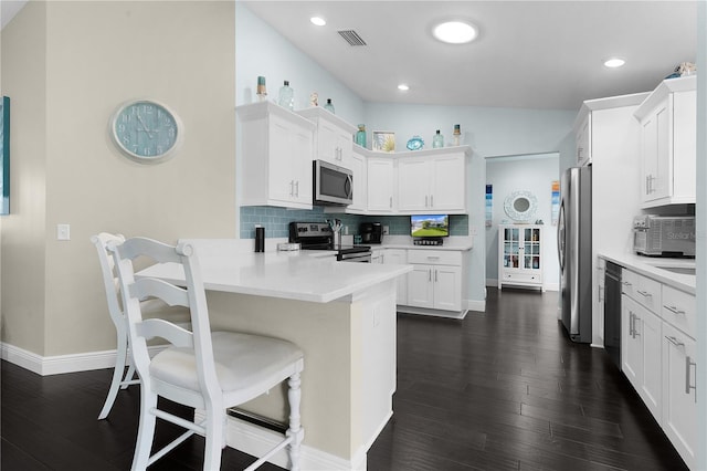 kitchen featuring white cabinetry, dark hardwood / wood-style flooring, kitchen peninsula, decorative backsplash, and appliances with stainless steel finishes