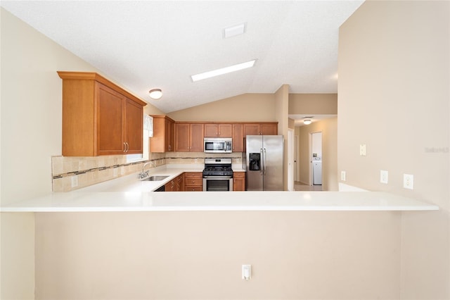 kitchen with kitchen peninsula, washer / clothes dryer, vaulted ceiling, and appliances with stainless steel finishes