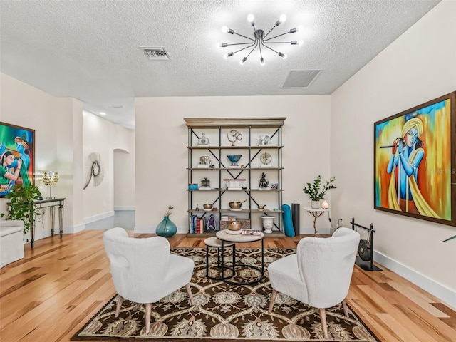 living area with a chandelier, wood-type flooring, and a textured ceiling