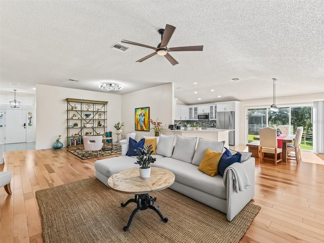 living room with a textured ceiling, light hardwood / wood-style flooring, and ceiling fan