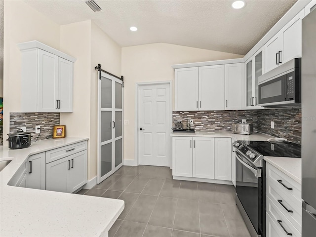 kitchen featuring white cabinetry, a barn door, vaulted ceiling, stainless steel electric stove, and decorative backsplash