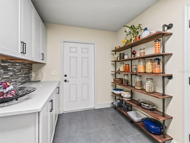 interior space featuring a textured ceiling, tasteful backsplash, white cabinetry, and dark tile patterned floors