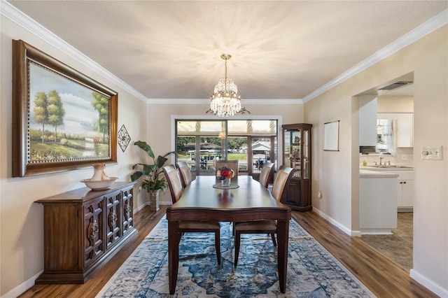 dining area with sink, crown molding, dark wood-type flooring, and an inviting chandelier