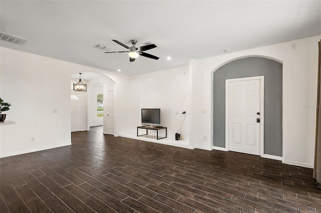 unfurnished living room with ceiling fan with notable chandelier and dark wood-type flooring