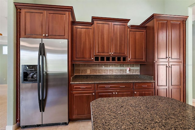 kitchen with light tile patterned floors, stainless steel refrigerator with ice dispenser, dark stone counters, and tasteful backsplash