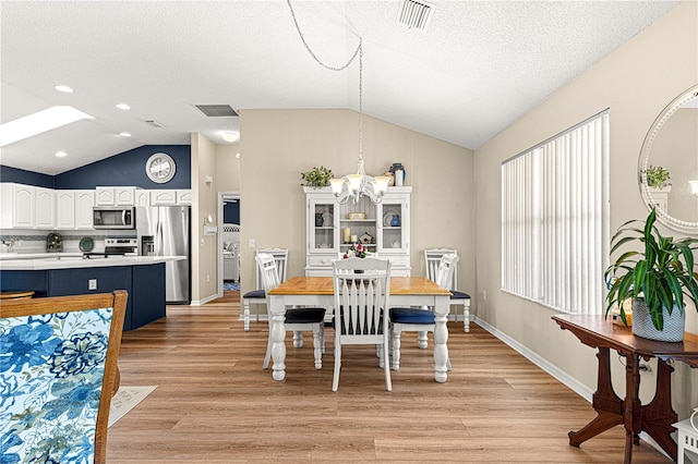 dining space featuring vaulted ceiling with skylight, light hardwood / wood-style floors, a textured ceiling, and an inviting chandelier