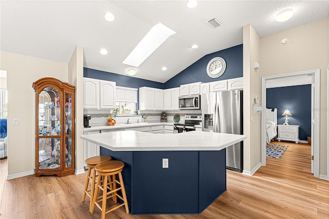 kitchen with a skylight, light wood-type flooring, appliances with stainless steel finishes, a kitchen island, and white cabinetry