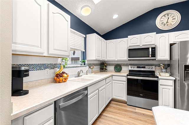 kitchen featuring appliances with stainless steel finishes, white cabinetry, lofted ceiling, and sink