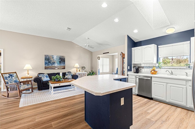 kitchen featuring white cabinetry, light hardwood / wood-style flooring, stainless steel dishwasher, vaulted ceiling with skylight, and a kitchen island