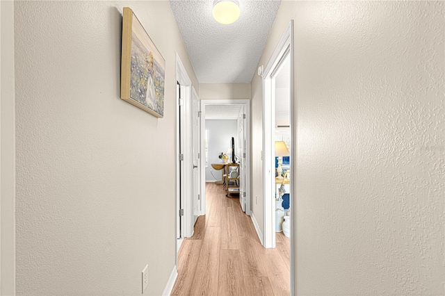 hallway with a textured ceiling and light hardwood / wood-style floors