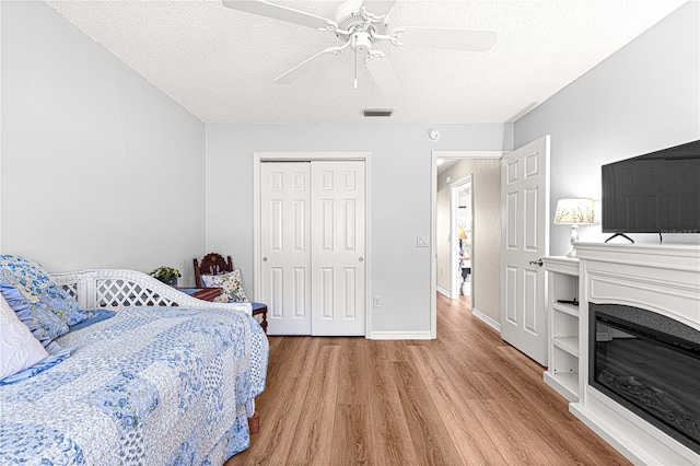 bedroom featuring ceiling fan, light hardwood / wood-style floors, a textured ceiling, and a closet