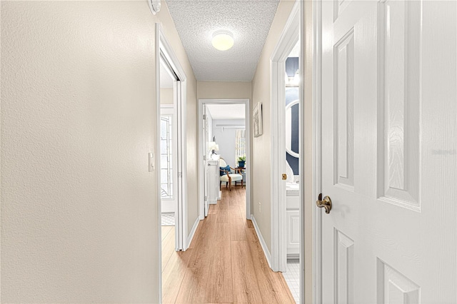 hall with a textured ceiling and light hardwood / wood-style floors