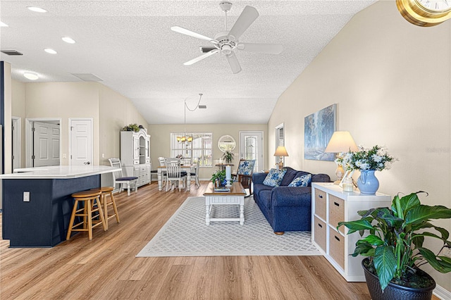 living room featuring lofted ceiling, light wood-type flooring, and ceiling fan with notable chandelier