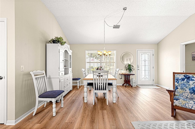 dining area featuring a chandelier, lofted ceiling, a textured ceiling, and light hardwood / wood-style flooring