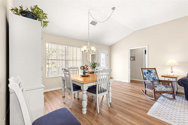 dining space with a textured ceiling, a chandelier, vaulted ceiling, and light wood-type flooring