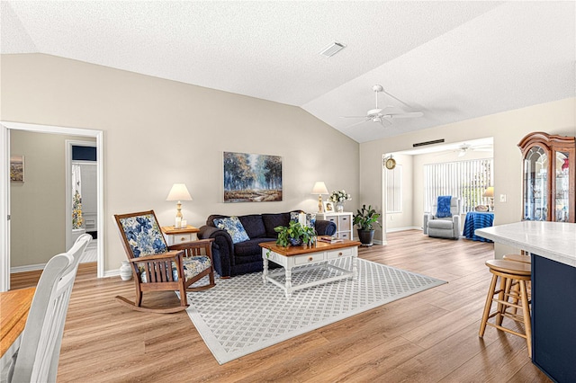 living room with a textured ceiling, light hardwood / wood-style floors, vaulted ceiling, and ceiling fan