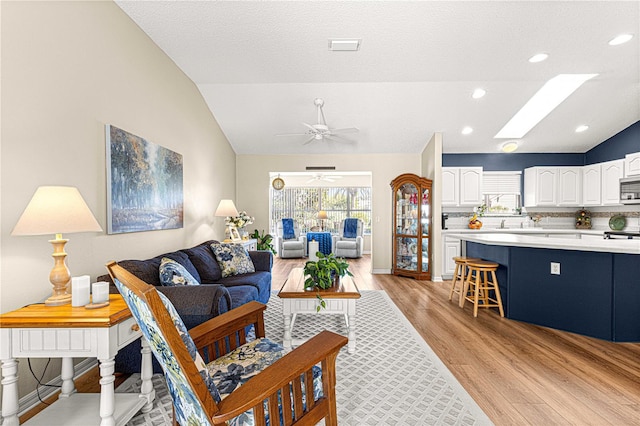 living room with light wood-type flooring, ceiling fan, and vaulted ceiling with skylight