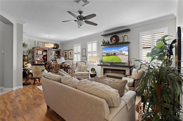 living room featuring wood-type flooring, a textured ceiling, ceiling fan, and ornamental molding