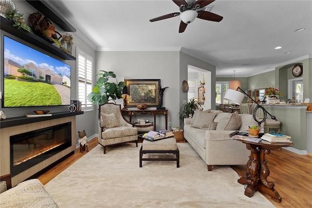 living room featuring a tile fireplace, ornamental molding, light wood-type flooring, and a healthy amount of sunlight