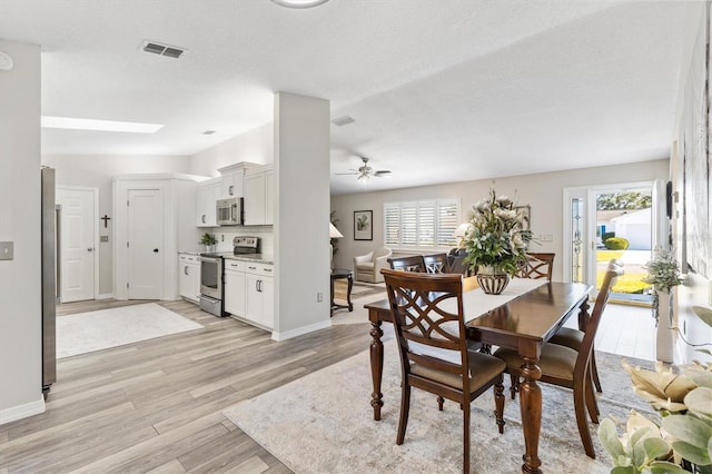 dining space featuring a skylight, light hardwood / wood-style flooring, ceiling fan, and a healthy amount of sunlight