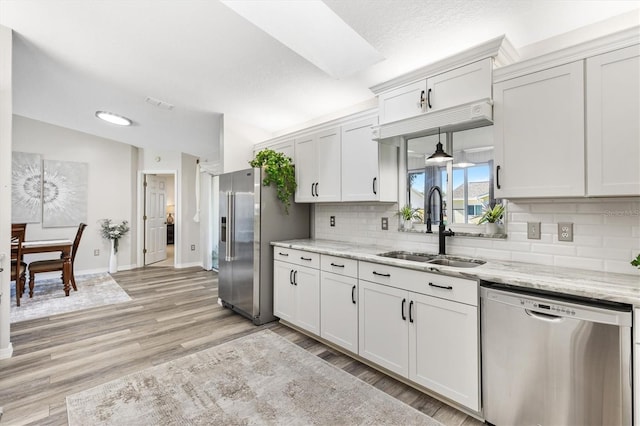 kitchen featuring sink, appliances with stainless steel finishes, light hardwood / wood-style floors, light stone counters, and white cabinetry