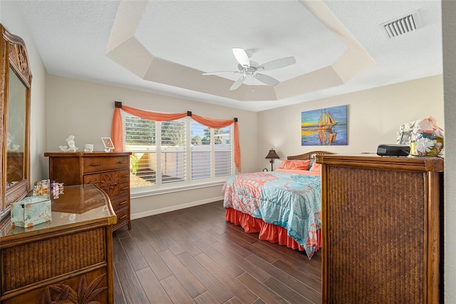 bedroom featuring a textured ceiling, dark hardwood / wood-style flooring, a tray ceiling, and ceiling fan