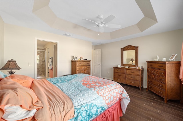 bedroom featuring a raised ceiling, ensuite bath, ceiling fan, and dark hardwood / wood-style flooring